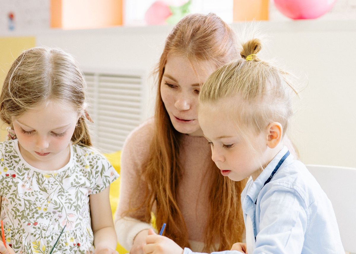 A childcare professional playing with children at a nursery table